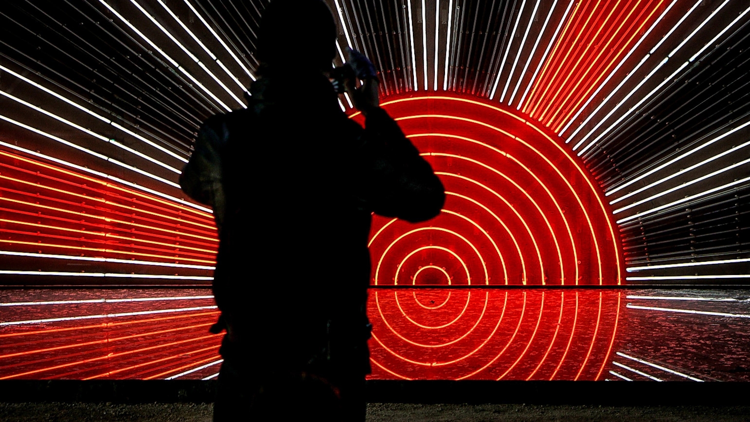 A shadowy figure stands with their back to the camera taking a shot of a light installation shaped like the Japanese imperial flag