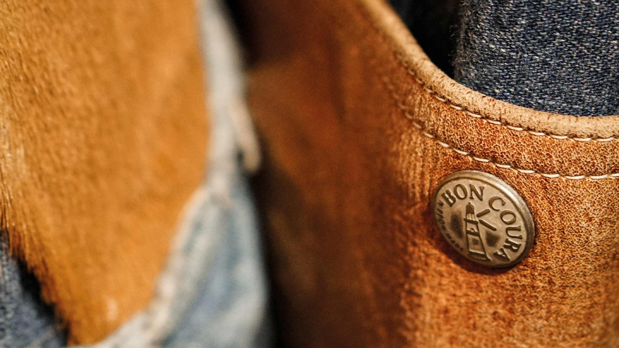 Bespoke BONCOURA button with the label's lighthouse logo, appears on a leather and denim item in Salon BONCOURA