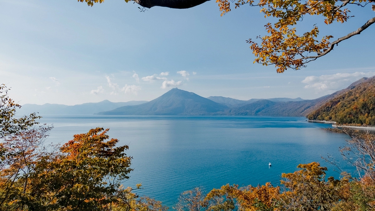 Autumnal leaves surround the edge of a photograph with a blue lake circled with mountains in the background