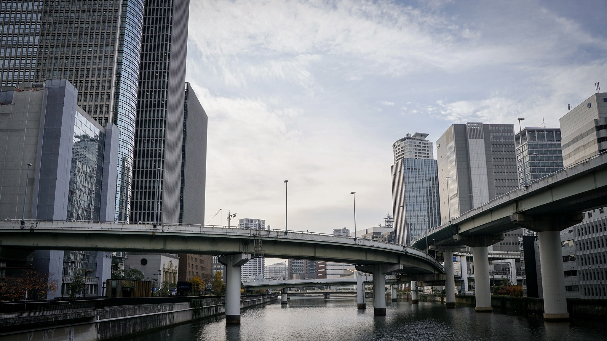 High rise buildings and a network of bridges typical of the cityscape of Osaka are set against a cloudy, blue winter's sky